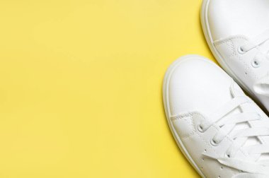 Sarı arka planda beyaz spor ayakkabılar düz yerde yatıyordu. Şık genç kadın deri ayakkabıları, spor ayakkabıları, hakiki deri ayakkabılar. Minimalist ayakkabı mağazası reklamcılığı moda ayakkabısı arka planı.