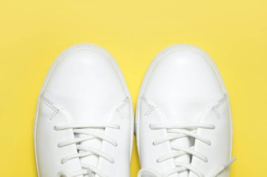 Sarı arka planda beyaz spor ayakkabılar düz yerde yatıyordu. Şık genç kadın deri ayakkabıları, spor ayakkabıları, hakiki deri ayakkabılar. Minimalist ayakkabı mağazası reklamcılığı moda ayakkabısı arka planı.