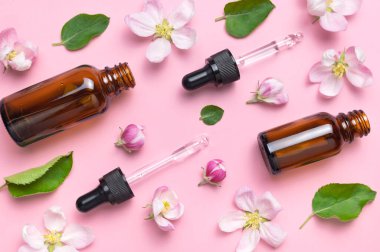 Damlatıcısı olan temiz kahverengi cam kozmetik şişeleri pembe arka planda narin bahar çiçekleri düz bir görünüm sergiliyordu. Bahar konsepti, doğal organik kozmetik ürünleri, güzellik ürünü spa yağı. Model.