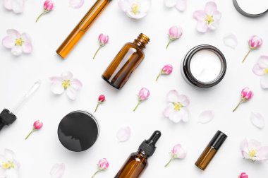 Doğal organik kozmetik bahar konsepti. Beyaz zemin üzerinde damlatan, kremalı, narin bahar çiçekleri olan temiz kahverengi cam kozmetik şişeleri düz bir zemin üzerinde yatıyordu. Güzellik bitkisi aromalı spa yağı..