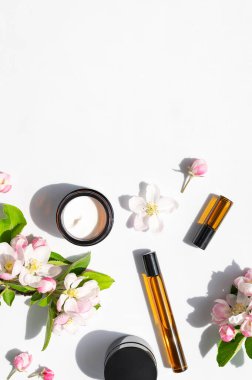 Doğal organik kozmetik bahar konsepti. Beyaz zemin üzerinde damlatan, kremalı, narin bahar çiçekleri olan temiz kahverengi cam kozmetik şişeleri düz bir zemin üzerinde yatıyordu. Güzellik bitkisi aromalı spa yağı..