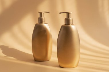 Bej arka planda güneş gölgeleri olan altın gibi temiz kozmetik şişeleri. Kozmetik şişeleri, tüpleri taklit ediyor. Marka ürünleri, spa, güzellik geçmişi. Düz görünüm kopyalama alanı yatıyordu. Tasarladığınız yer.