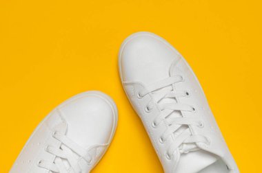 Sarı arka planda beyaz kadın deri spor ayakkabıları düz yerde yatıyordu. Şık gençlik ayakkabıları, spor ayakkabıları, hakiki deri ayakkabılar. Minimalist ayakkabı mağazası reklamcılığı moda ayakkabısı arka planı.
