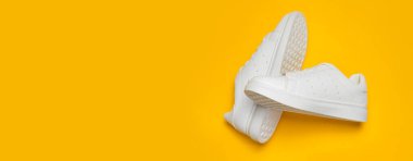 Sarı arka planda beyaz kadın deri spor ayakkabıları düz yerde yatıyordu. Şık gençlik ayakkabıları, spor ayakkabıları, hakiki deri ayakkabılar. Minimalist ayakkabı mağazası reklamcılığı moda ayakkabısı arka planı.