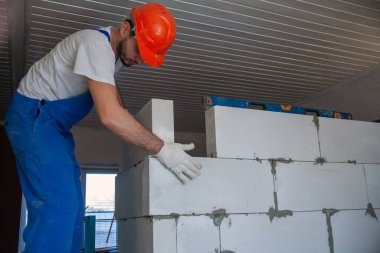 Mason, inşa edilmiş ev duvarının havalandırmalı beton bloğunu hizalıyor.