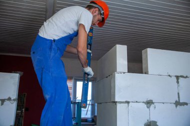 Mason, inşa edilmiş ev duvarının havalandırmalı beton bloğunu hizalıyor.