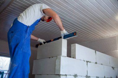 Mason, inşa edilmiş ev duvarının havalandırmalı beton bloğunu hizalıyor.