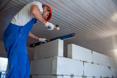 Mason, inşa edilmiş ev duvarının havalandırmalı beton bloğunu hizalıyor.