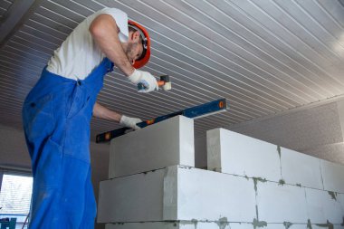 Mason, inşa edilmiş ev duvarının havalandırmalı beton bloğunu hizalıyor.