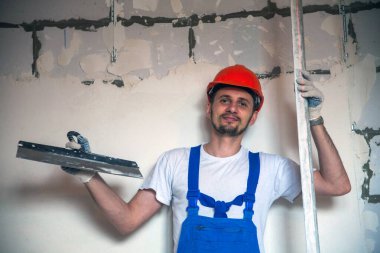 Yüksek katlı binanın ön cephesini macun bıçağıyla kaplayan inşaat işçisi.