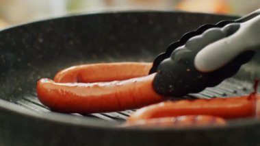 Aşçı ızgarada sosis pişiriyor.