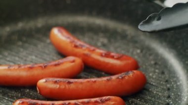 Aşçı ızgarada sosis pişiriyor.