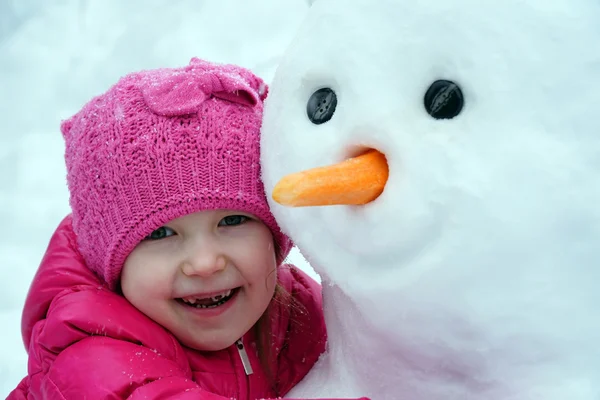 Niña abrazando a un muñeco de nieve grande — Foto de Stock