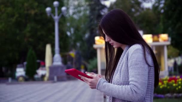 Κορίτσι που κάθεται σε ένα παγκάκι σε το πάρκο και χρήση εφαρμογών σε το υπολογιστή tablet — Αρχείο Βίντεο