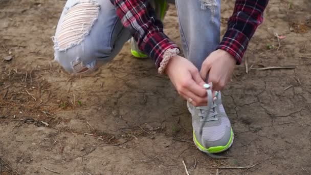 Young girl commits an outdoor walk and stopped to tie his shoelaces on sneakers — Stock Video