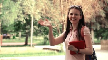 parkta yürüyüş ve kameraya sallayarak görüntüleri genç güzel kadın. Öğrenci elinde bir tablet.