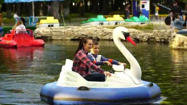 Metraje joven mujer y un adolescente flotan en un cisne inflable en el lago en el parque. 4K — Vídeo de stock