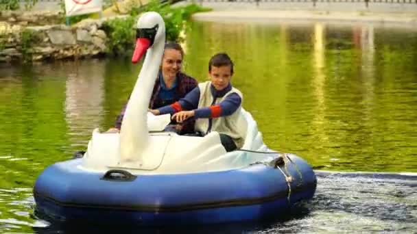 映像若い女性およびティーネー ジャーは、公園で湖の上の膨脹可能なスワンを浮遊します。4 k — ストック動画