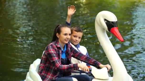 Кадри молодої жінки і підлітка плавають на надувному лебеді на озері в парку. 4-кілометровий — стокове відео