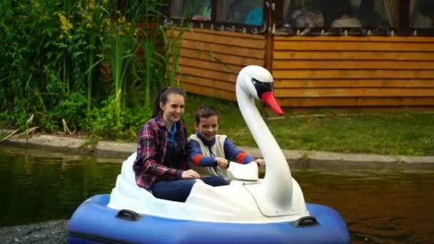 Metraje joven mujer y un adolescente flotan en un cisne inflable en el lago en el parque. 4K — Vídeo de stock