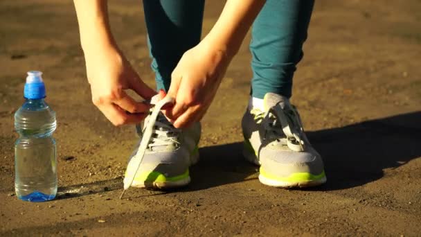 Meisje gestopt om te binden de veters op loopschoenen. Fitness meisje opleiding buitenshuis. 4k — Stockvideo