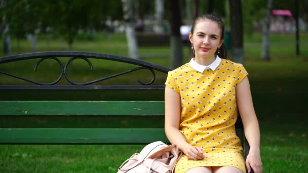 Žena sedí na lavičce v parku a při pohledu na fotoaparát — Stock video