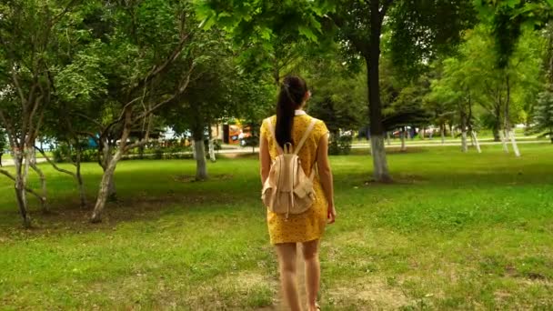 Запись женщины, гуляющей в парке с рюкзаком. 4K — стоковое видео