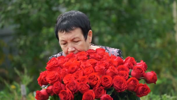 Μήκος σε πόδηα ηλικιωμένη γυναίκα, κρατώντας ένα μπουκέτο τριαντάφυλλα σε εξωτερικούς χώρους. 4k — Αρχείο Βίντεο