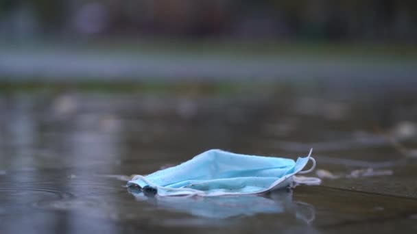 Mascarilla desechable usada en charco durante la lluvia — Vídeo de stock