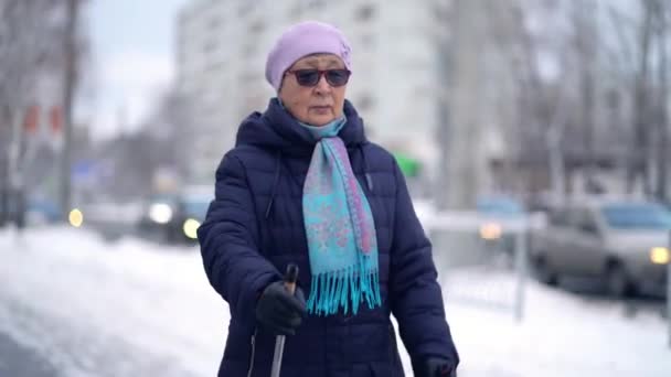 Wanita lanjut usia yang aktif melatih Nordic berjalan dengan tiang trekking. Wanita tua berlatih berjalan keluar Nordic di musim dingin — Stok Video