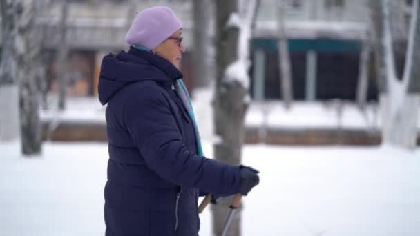 Actieve oudere vrouw traint Nordic walking met wandelstokken. Oudere vrouw die in de winter nordic walking beoefent — Stockvideo