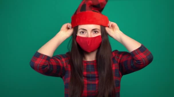 Mujer vistiendo máscara facial médica roja poniéndose sombrero de santa. — Vídeos de Stock