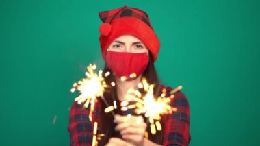 Havai fişek maytap ve Noel şapkalı güzel bir kadın. Coronavirus için koruyucu yüz maskesi takıyor.