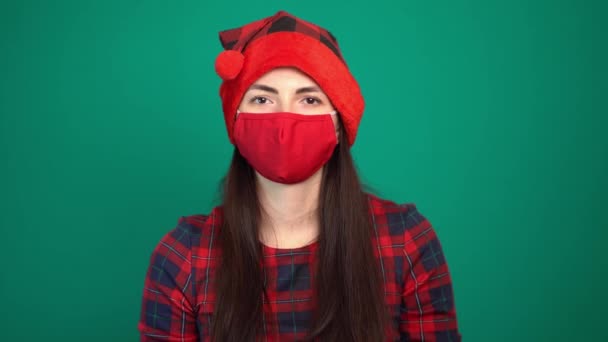 Retrato de una mujer bonita con sombrero rojo navideño y mascarilla médica protectora que muestra un gesto de cremallera en la boca — Vídeo de stock