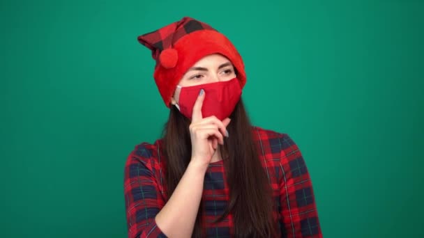 Kırmızı tıbbi maske ve Noel şapkası takan güzel bir kadın bir şeyin hayalini kuruyor. — Stok video