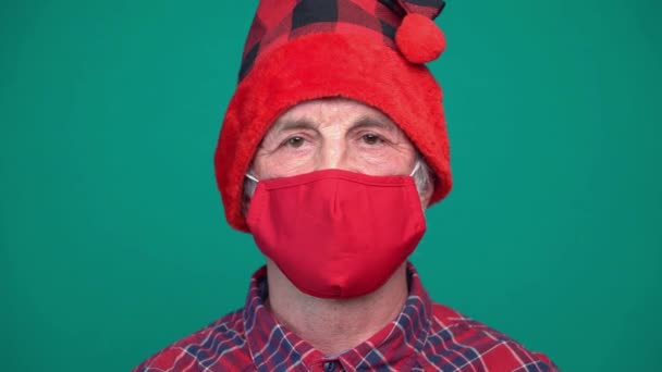 Kırmızı tıbbi maskeli ve Noel Baba şapkalı olgun bir adamın resmi, kameraya bakıyor. — Stok video