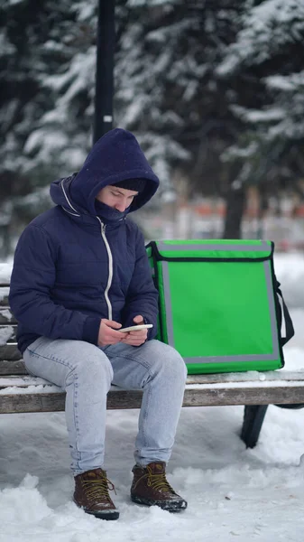 Bezorger met een geïsoleerde rugzak op zoek naar het adres van de klant in de bezorgapp — Stockfoto