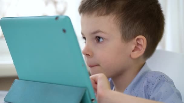 Przedszkolak siedzi przy stole i patrzy na cyfrowy tablet — Wideo stockowe