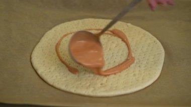 Kadın kepçeyle pizza hamuruna domates sosu sürüyor.