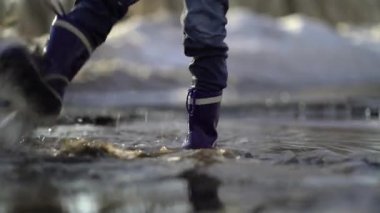 happy boy rubber boots have fun playing in a puddle, on road
