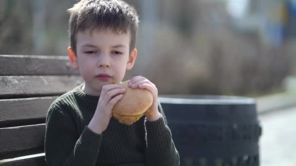 Aç çocuk dışarıda hamburger yiyor. — Stok video