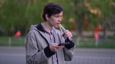 Adam akıllı telefonunda uygulama kullanıyor ve cam şişeden limonata içiyor.