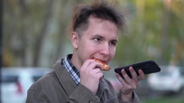 Niño comiendo pizza y enviar un mensaje de voz en el teléfono inteligente de la ciudad — Vídeo de stock