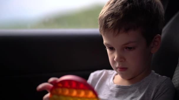 Niño jugando con popit arco iris o hoyuelo simple en el coche. Juguete de silicona moderno — Vídeos de Stock