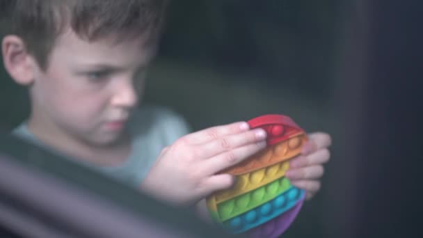 Niño jugando con popit arco iris o hoyuelo simple en el coche. Juguete de silicona moderno — Vídeos de Stock