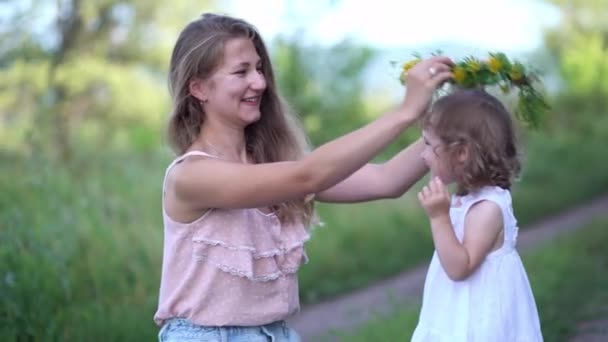 Mama kładzie wieniec z dzikich kwiatów na jej córki głowę w przyrodzie — Wideo stockowe