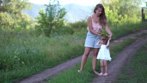Mama kładzie wieniec z dzikich kwiatów na jej córki głowę w przyrodzie — Wideo stockowe