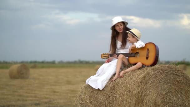 Embarazada mamá y su hijo tocar la guitarra y sentarse en el pajar en el campo — Vídeo de stock