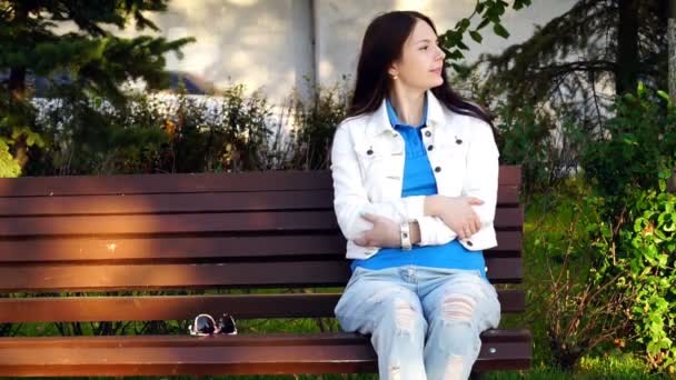 Красивая девушка сидит на скамейке в парке — стоковое видео