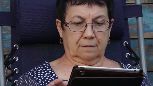 Woman sitting in the yard and enjoys the tablet — Stock Video